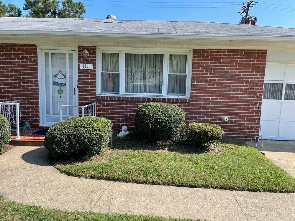 Brick house with small lawn, shrubs, and a white front door and garage door.