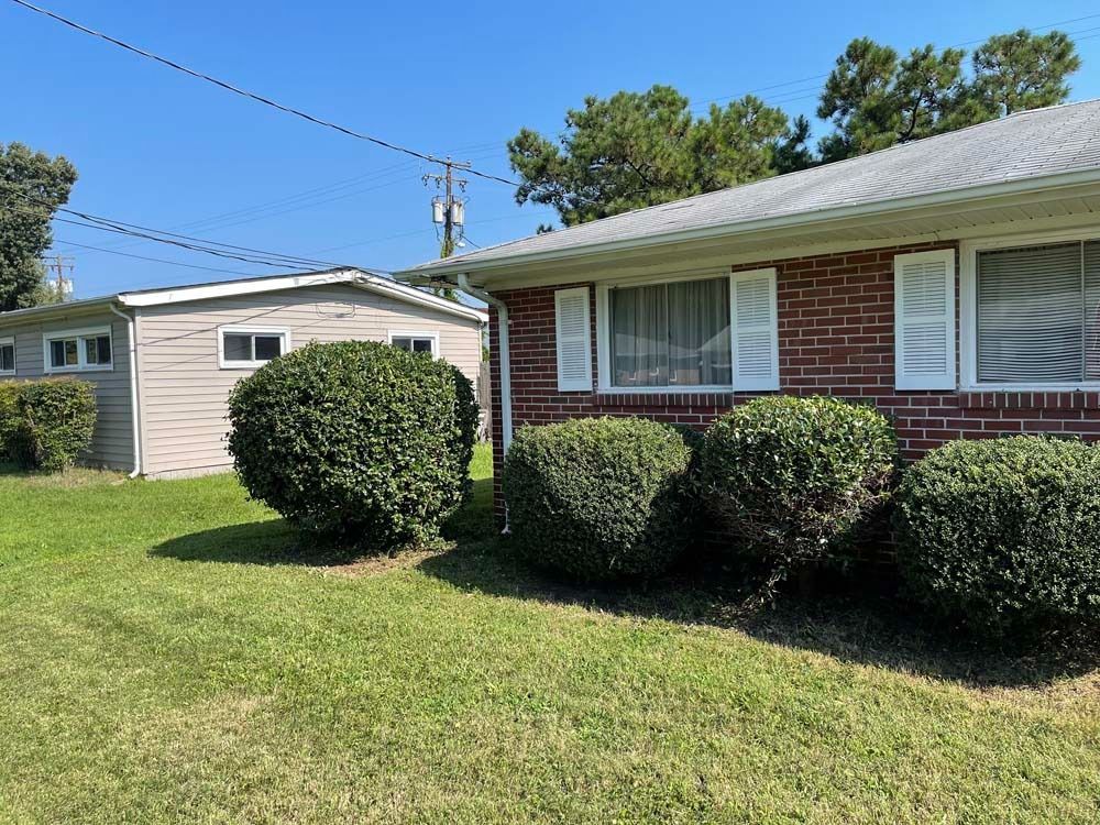 Brick house with white trim, green lawn, and shrubbery. A detached gray garage is to the left. Sunny day.