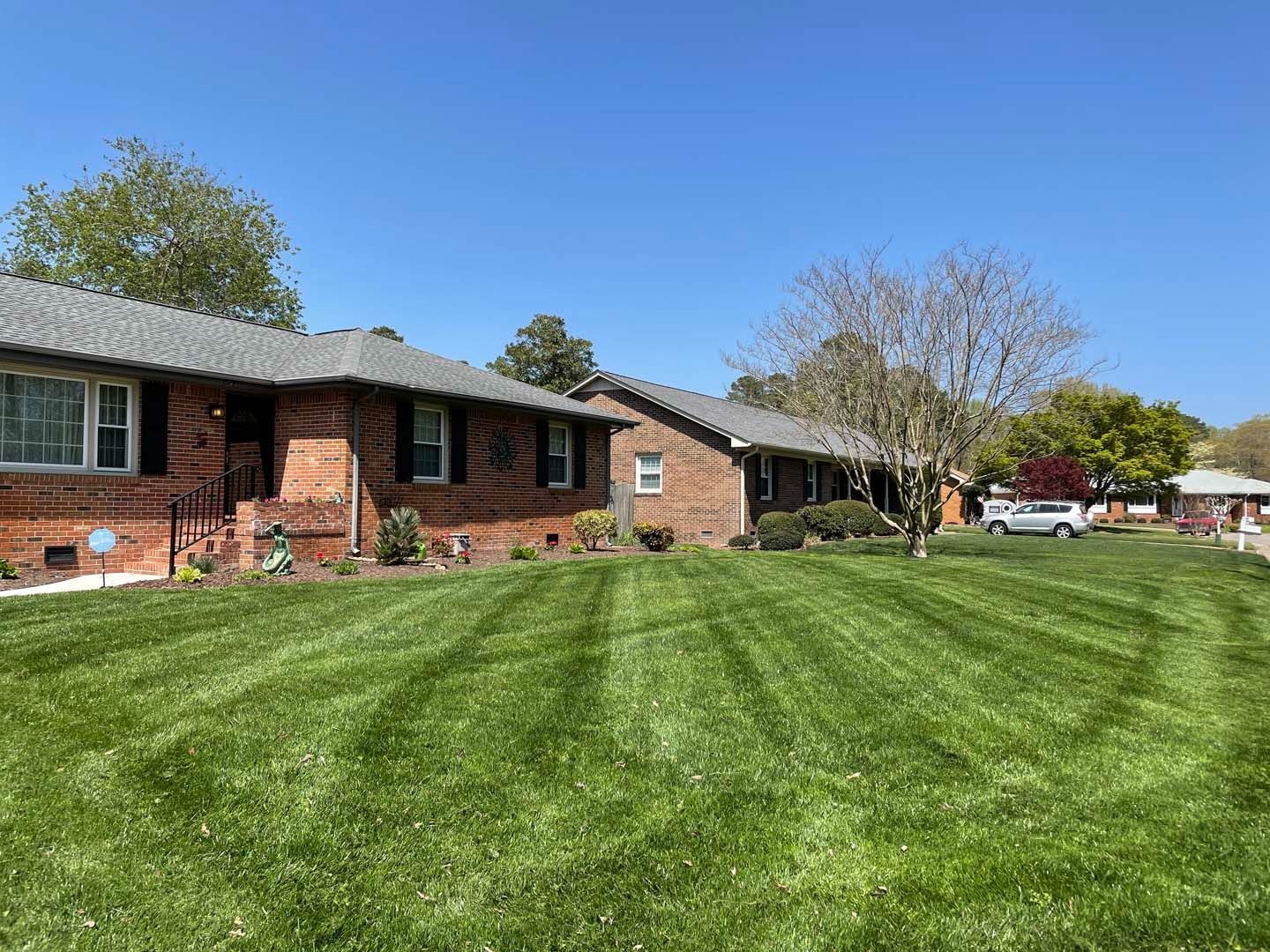 Row of brick homes with well-manicured green lawn under a clear, blue sky.