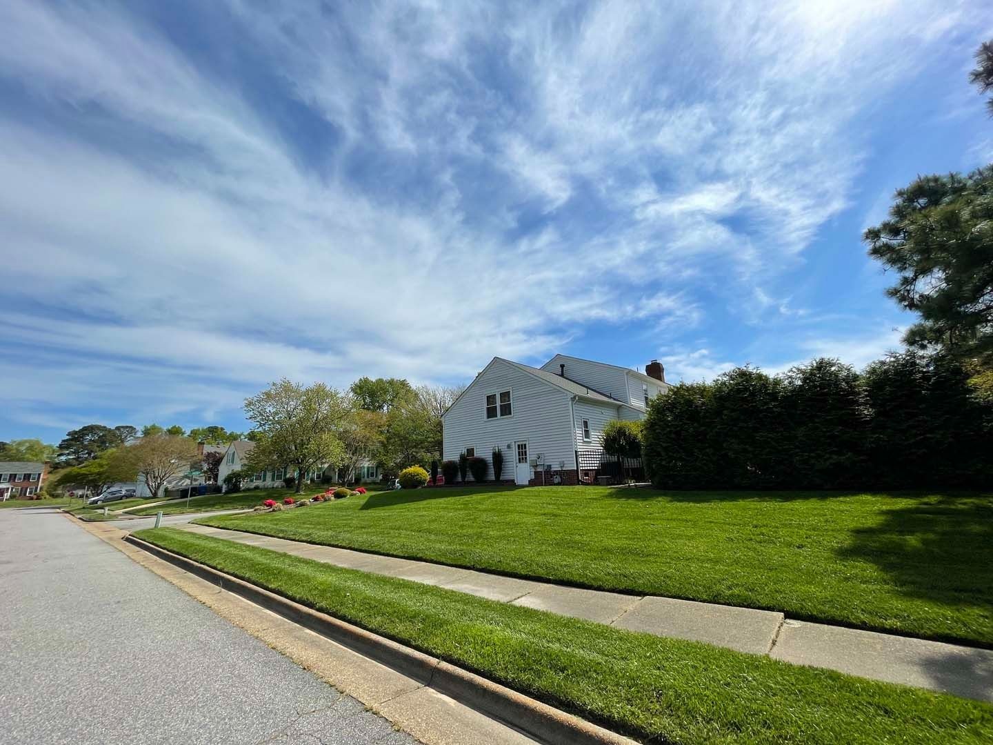 Street view of white house with lawn under a cloudy blue sky.