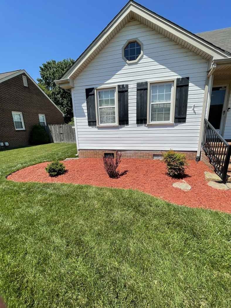 White house with black shutters, red mulch bed, green lawn, blue sky.