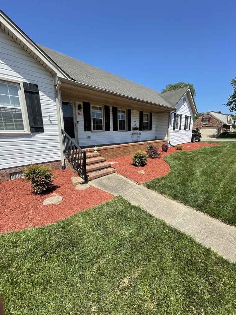 White house with a covered porch, black shutters, and red mulch in the landscaping.
