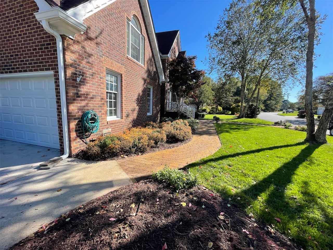 Brick house with a driveway, walkway, and garden bed. Green grass, blue sky.