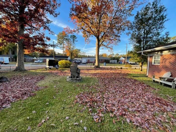 Yard with fallen red leaves, trees, brick house, and clear blue sky in autumn.