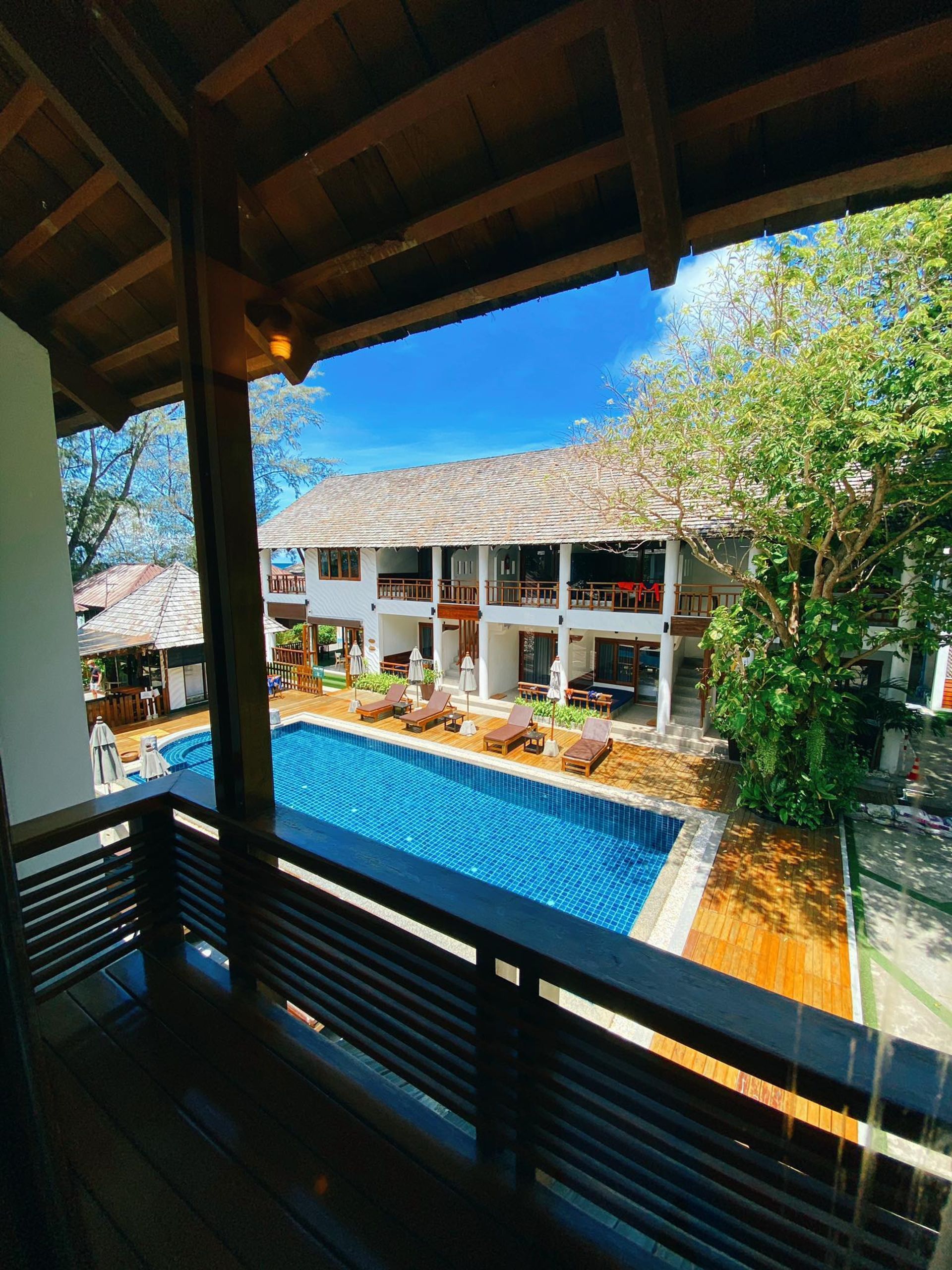 Balcony view of a pool and a white multi-story building with wooden accents.