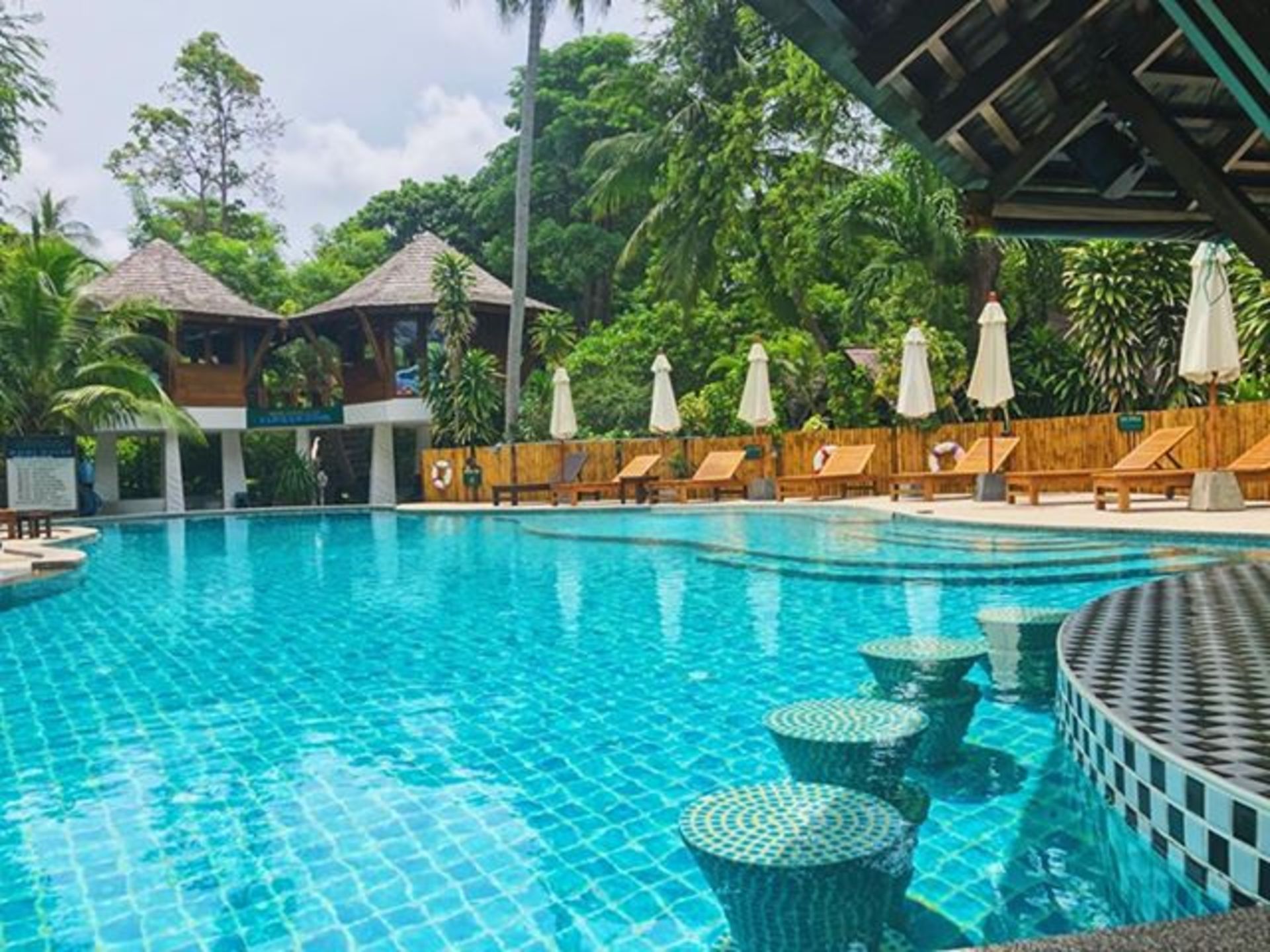 Swimming pool at a resort with pool bar stools, lounge chairs, and two treehouse-like structures.