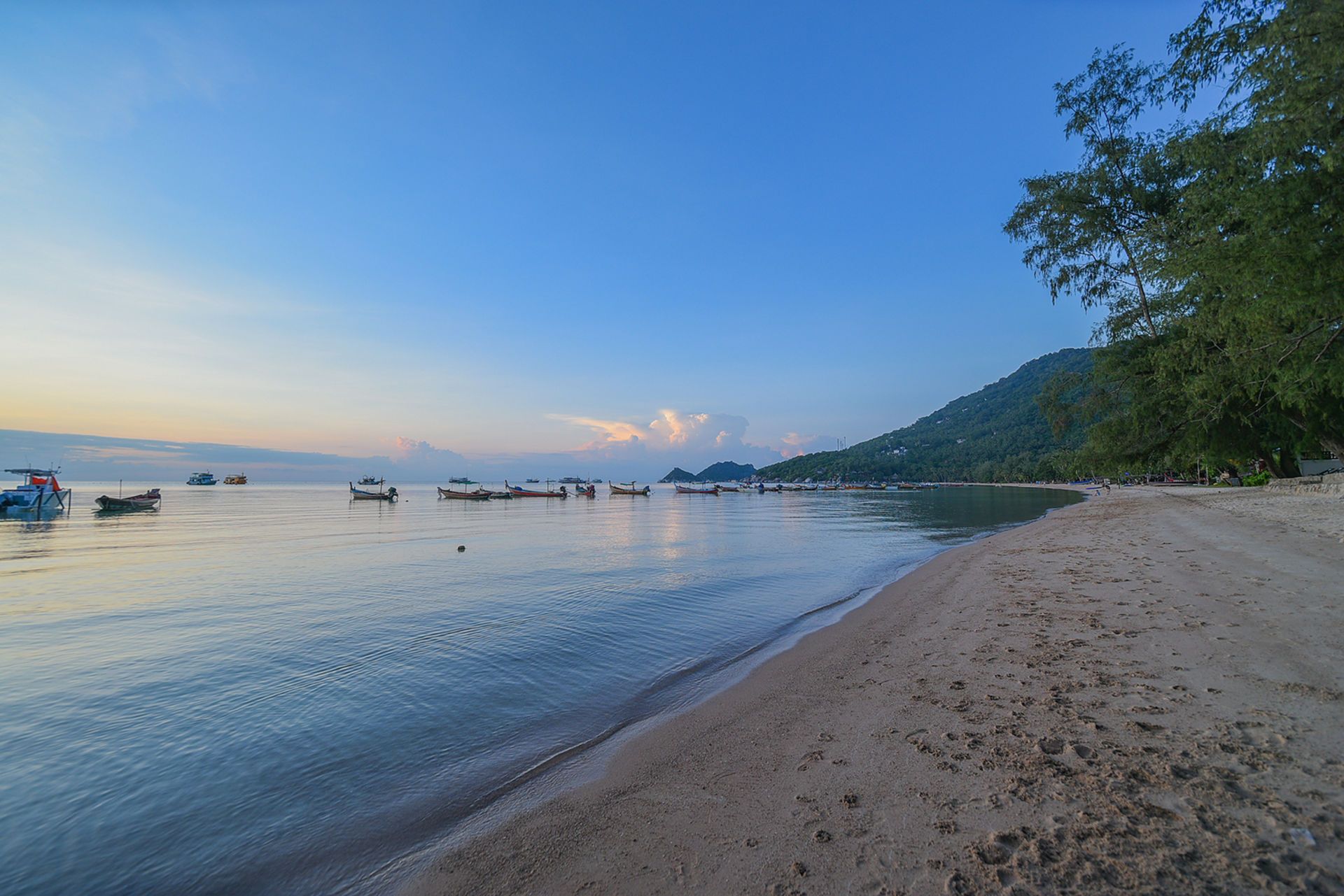 Sandy beach with boats in calm water, under a blue and dusky sky.
