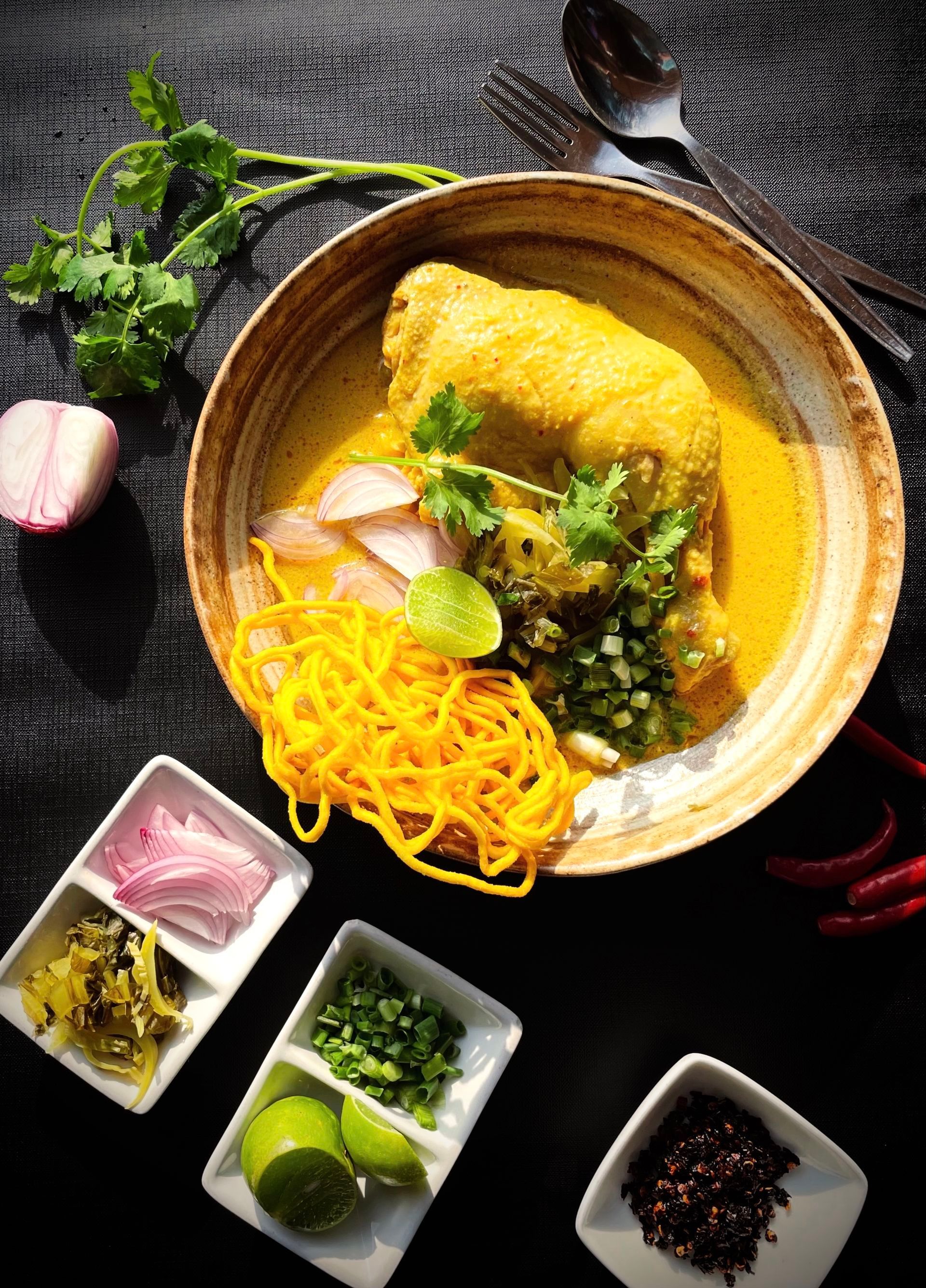 Khao Soi: Yellow curry noodle soup with chicken in a wooden bowl, garnished with cilantro and lime.