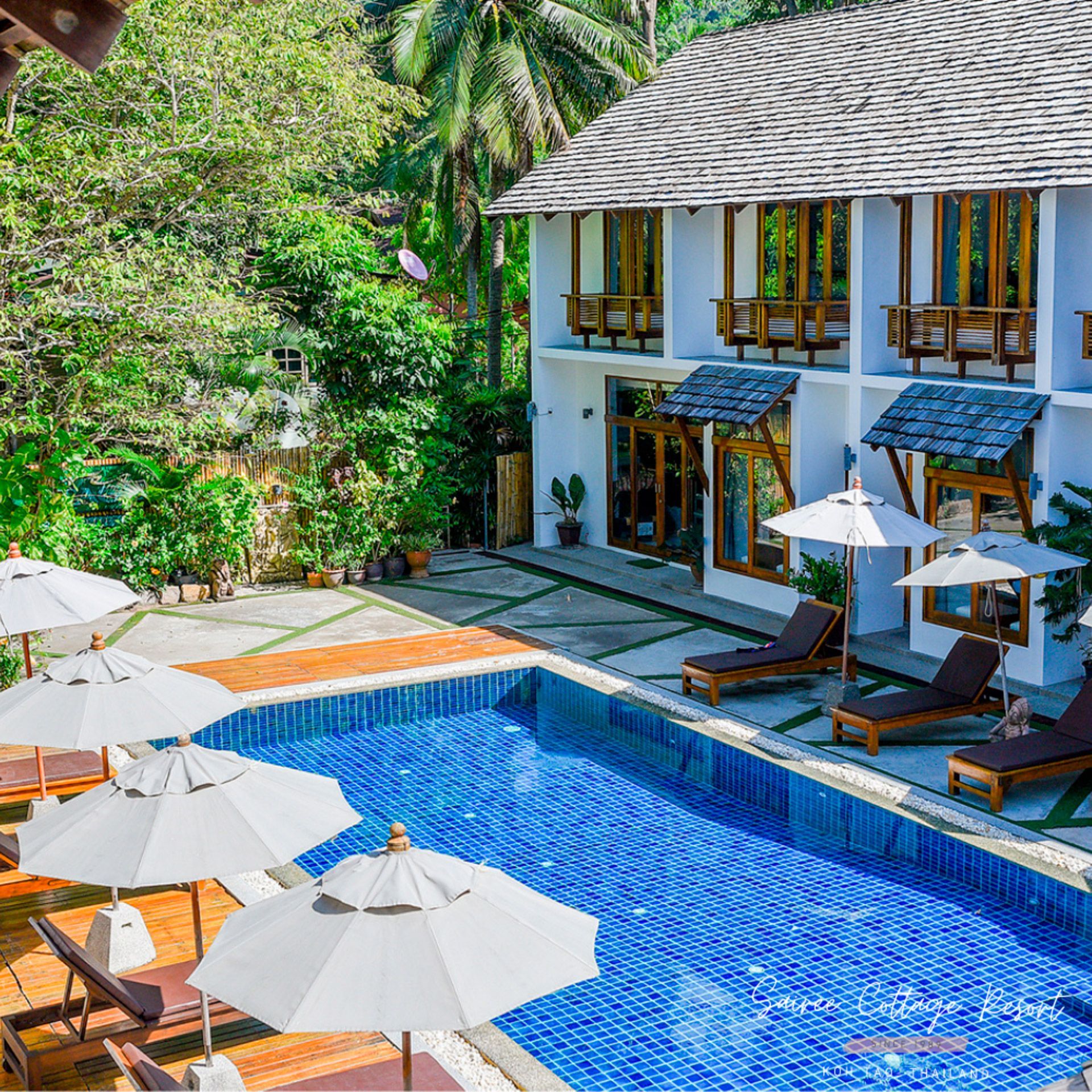 Swimming pool and lounge chairs near a white, two-story building with wooden accents.