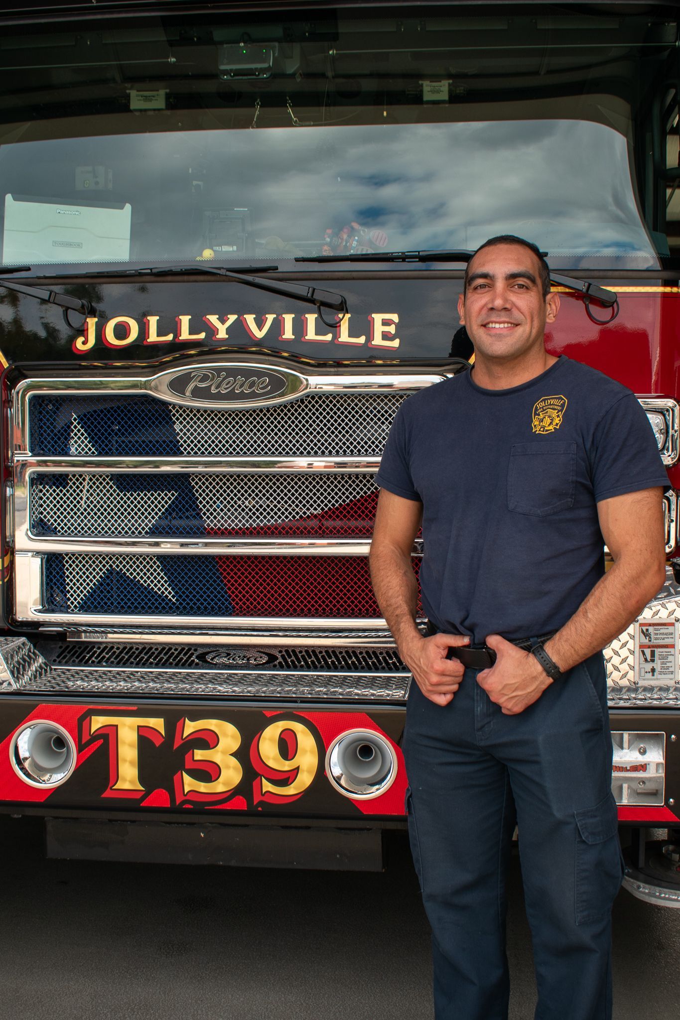 A firefighter in a polo shirt is standing in front of a fire engine.