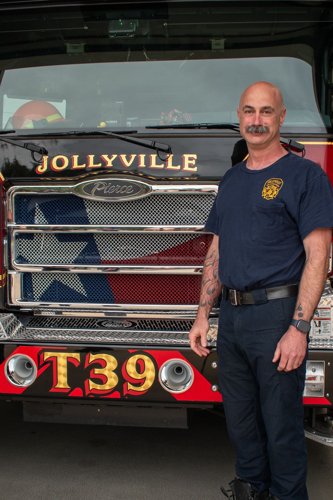 A man is standing in front of a fire engine with his arms crossed.