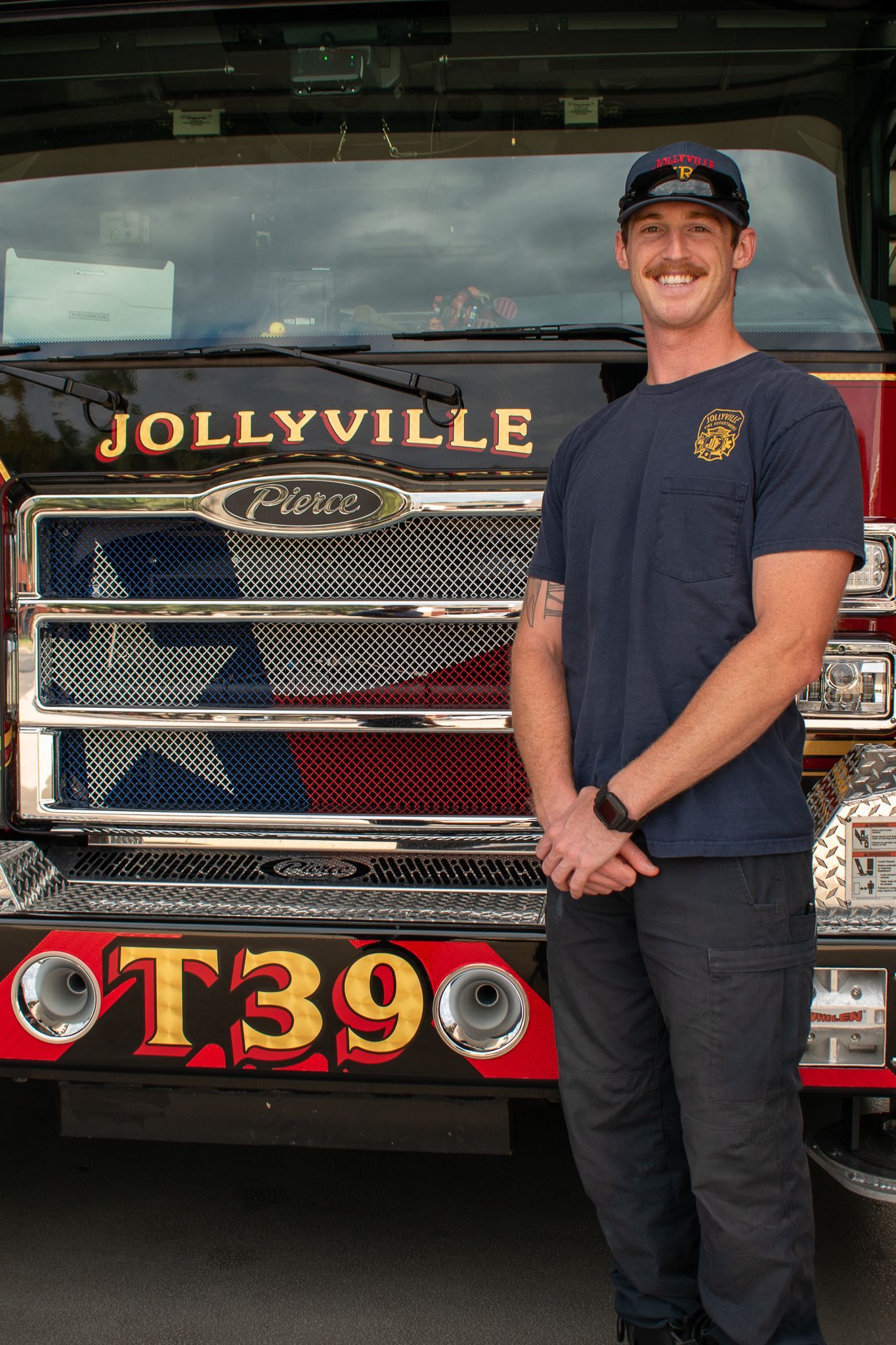 A firefighter in a polo shirt is standing in front of a fire engine.