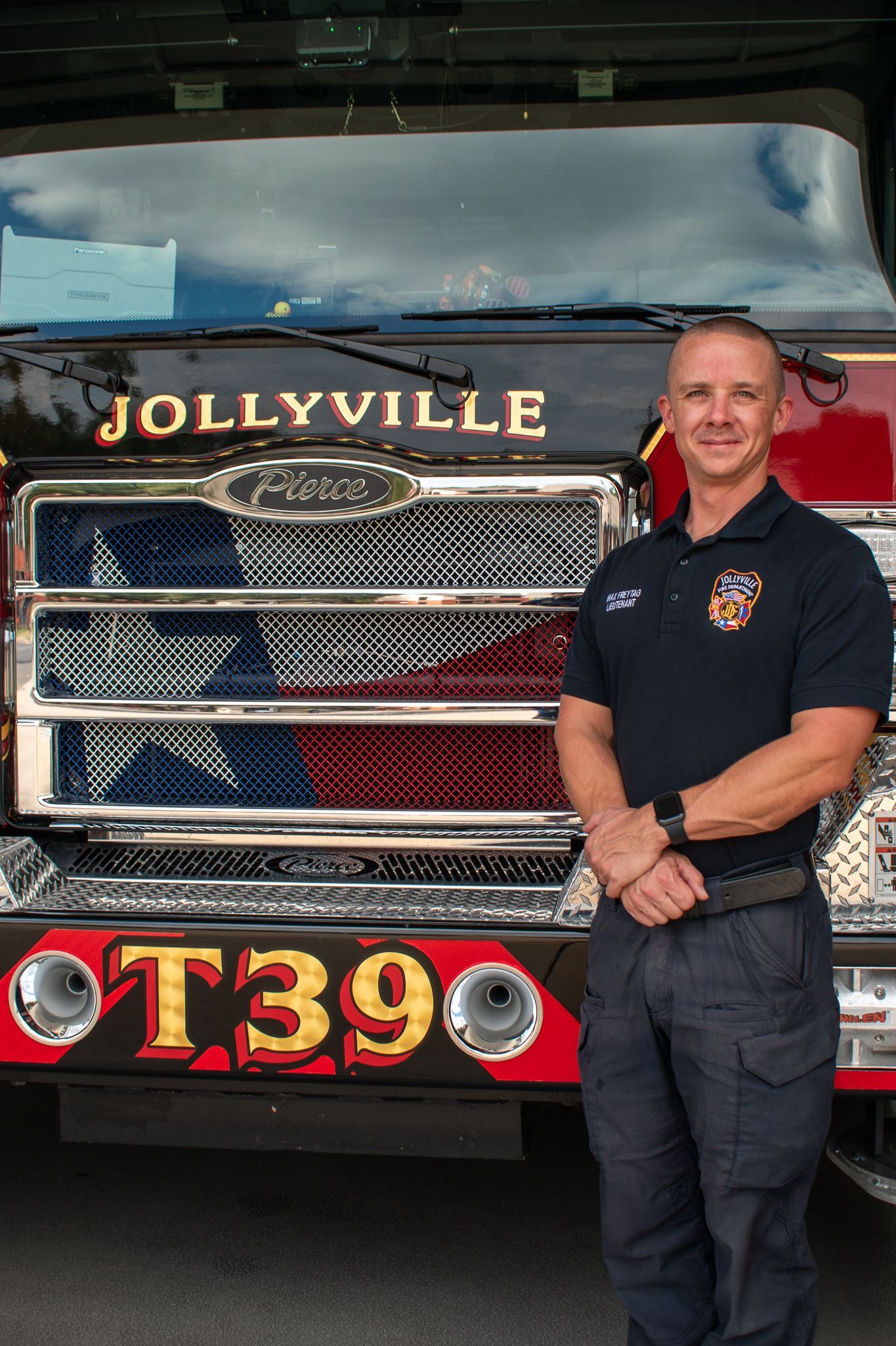 A firefighter in a polo shirt is standing in front of a fire engine.