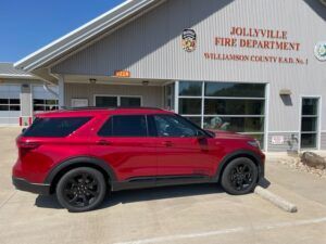 A red suv is parked in front of a fire department building.