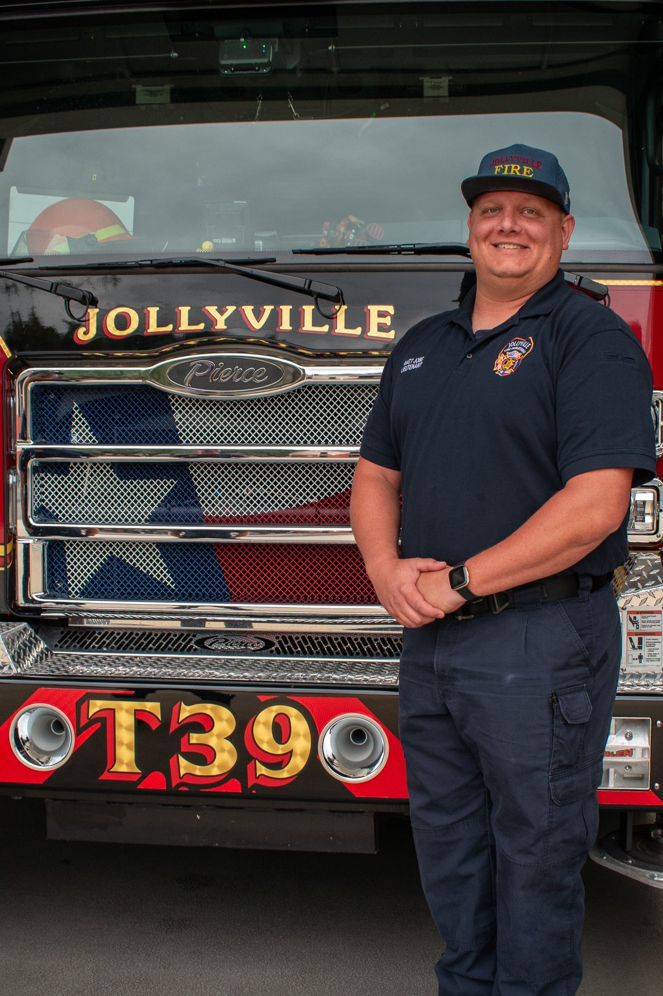 A firefighter in a polo shirt is standing in front of a fire engine.