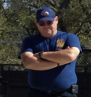 A man in a blue shirt and hat is standing with his arms crossed.