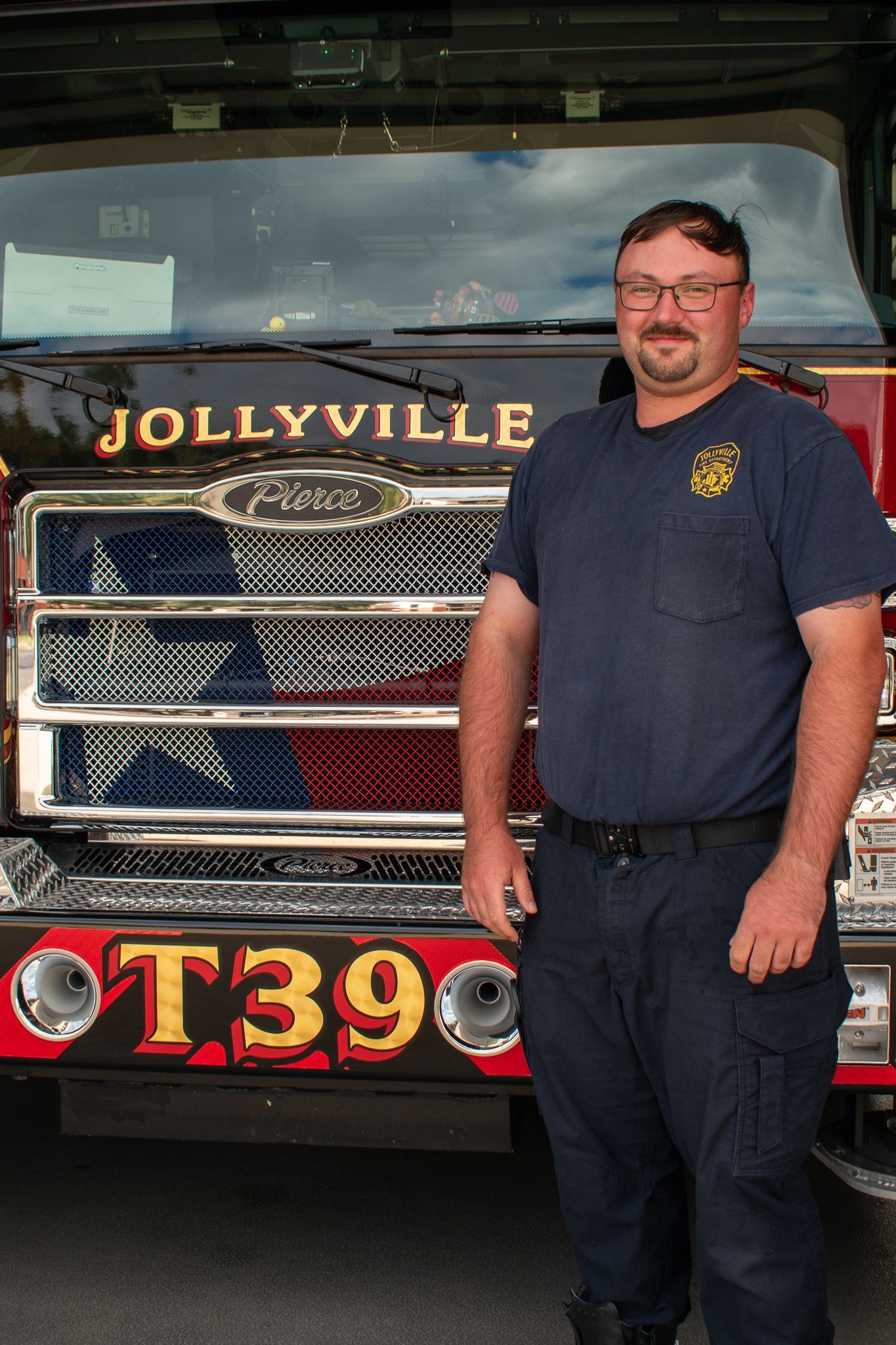 A firefighter in a polo shirt is standing in front of a fire engine.