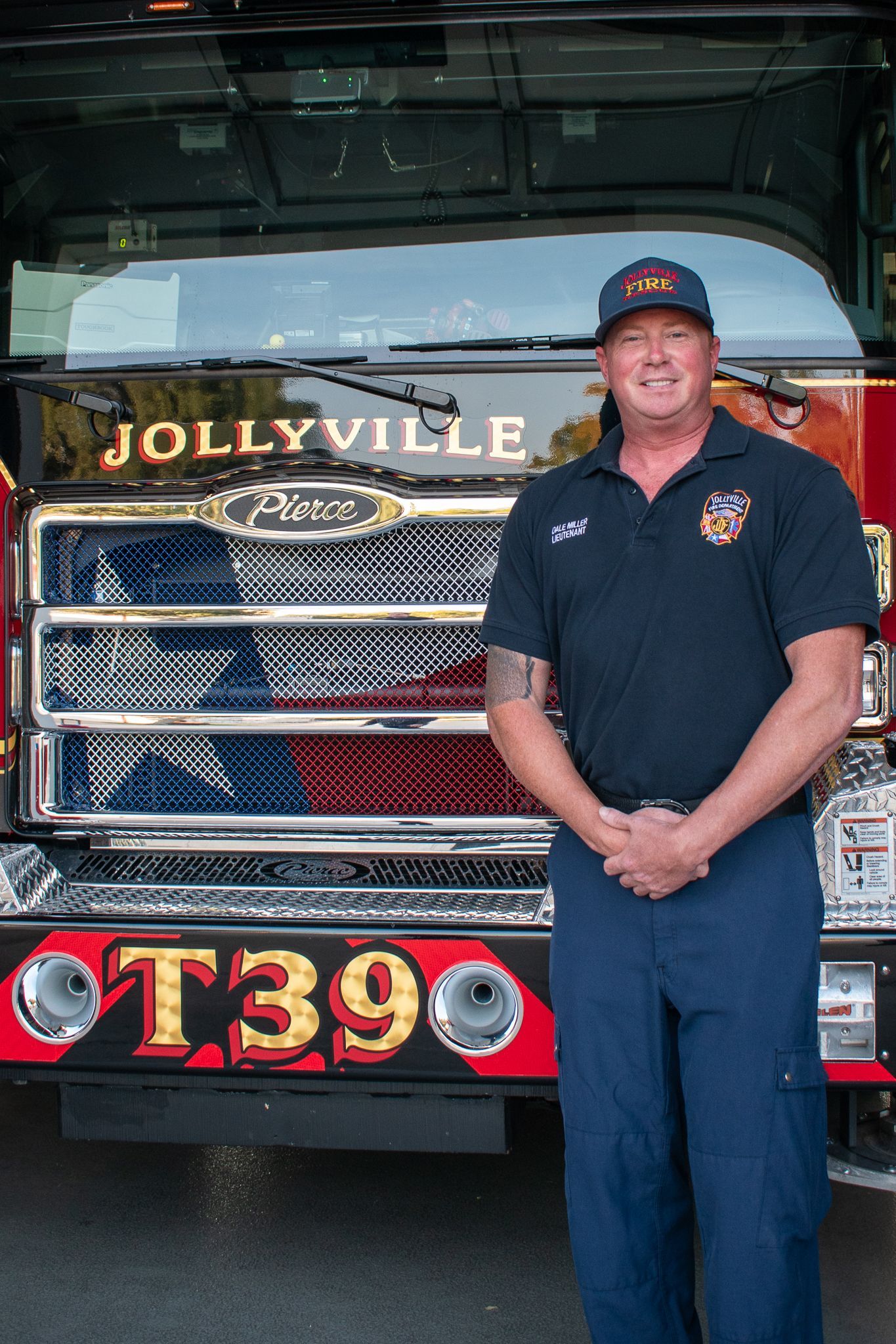 A firefighter in a polo shirt is standing in front of a fire engine.