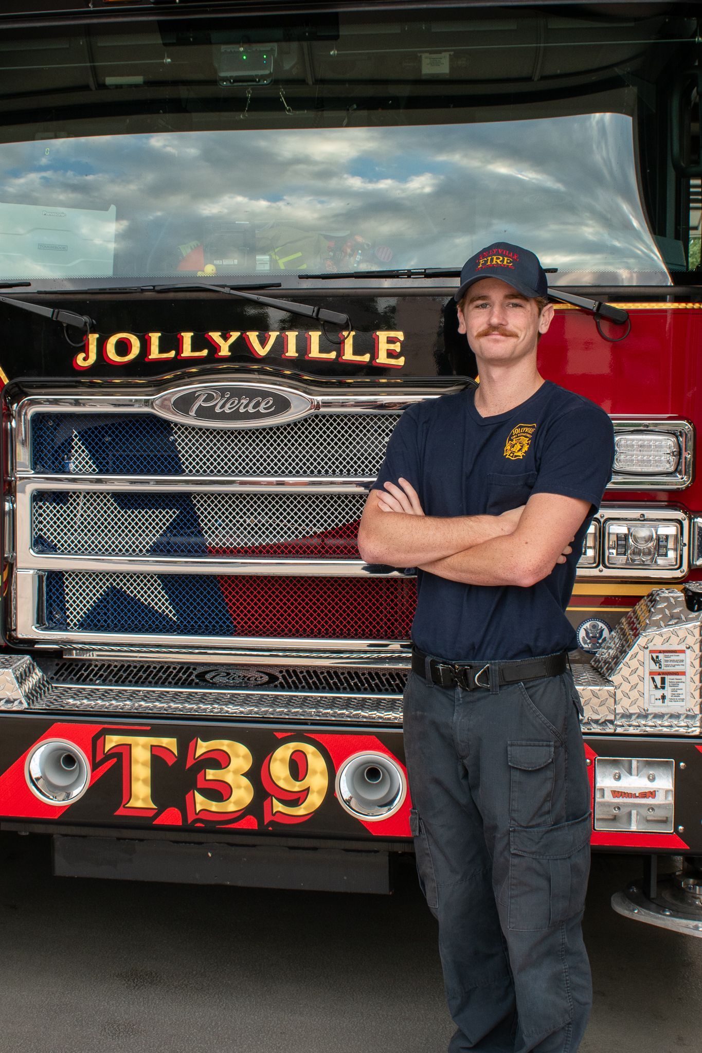 A man is standing in front of a fire engine with his arms crossed.