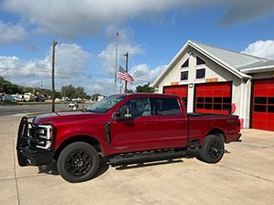 A red pickup truck is parked in front of a fire station.