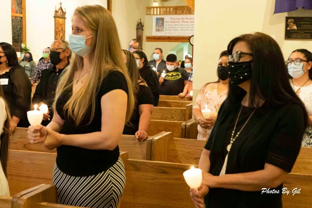 People gathered in a church, wearing masks, holding candles during a solemn vigil. 