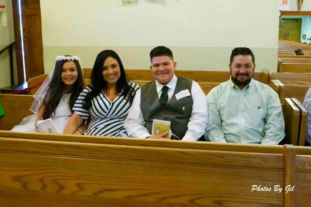 A family of four smiling, seated in church pews.