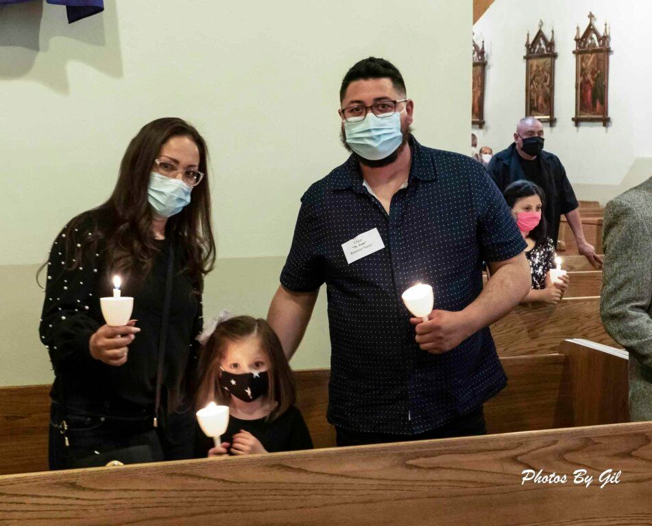 A family of three wearing face masks stands in a church, holding candles during a ceremony.