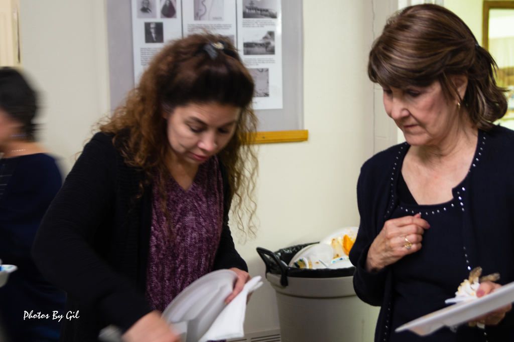 Two women holding plates stand near a wall with posters. 