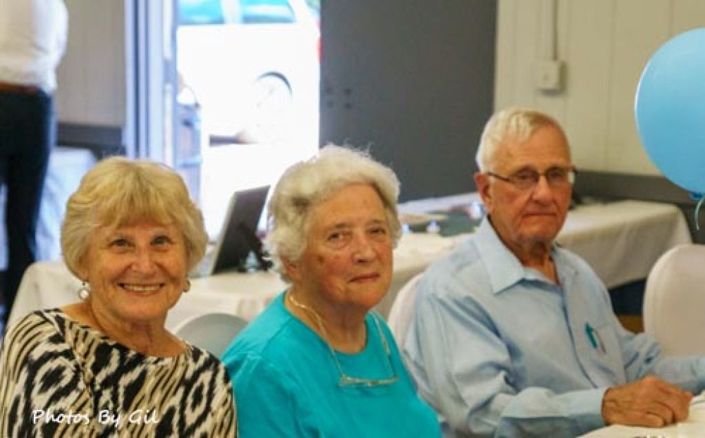 Three elderly individuals sit together at a table, smiling warmly.