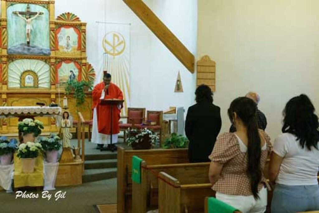 A priest in a red robe stands at the altar reading from a lectern in a church. 