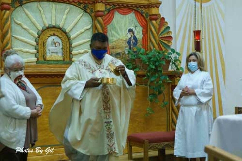 A priest in ornate robes, wearing a blue mask, holds a chalice in a church. 
