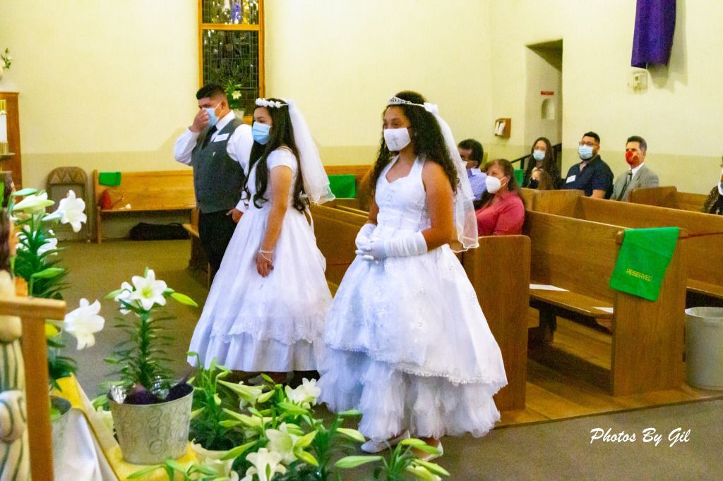 Two girls in white dresses and veils stand in a church, wearing masks.