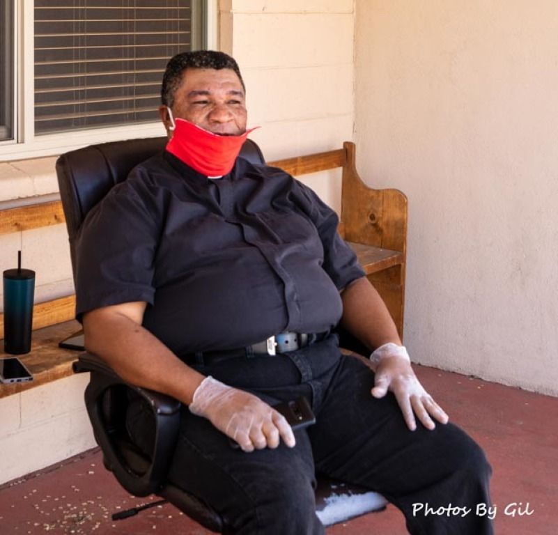Man in a black outfit sits on a chair, wearing a red mask.