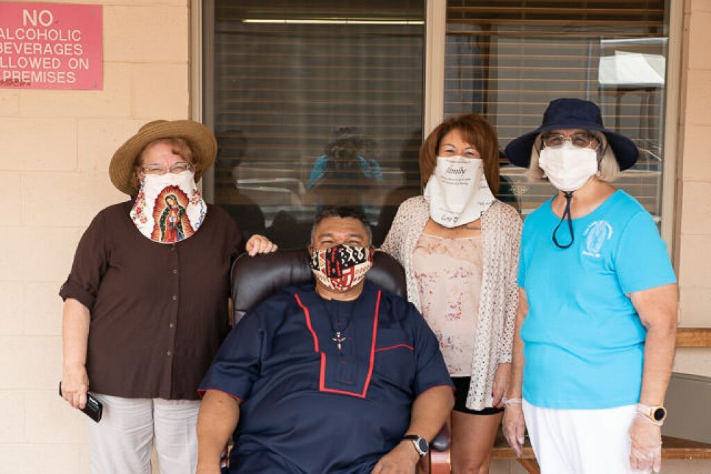 Four people, three standing and one seated, wearing decorative face masks in an outdoor setting.
