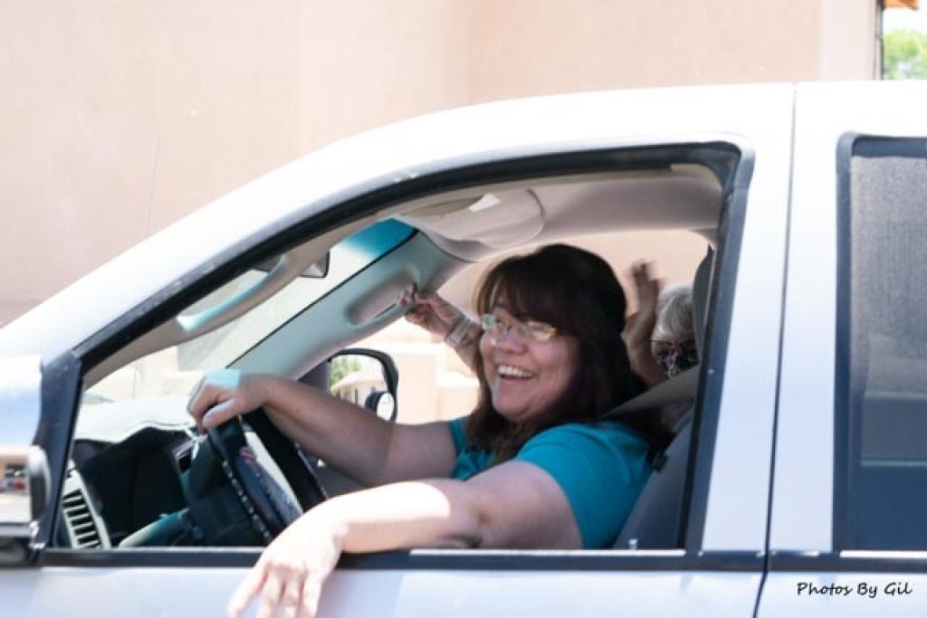 A woman joyfully drives a white vehicle, smiling broadly. 