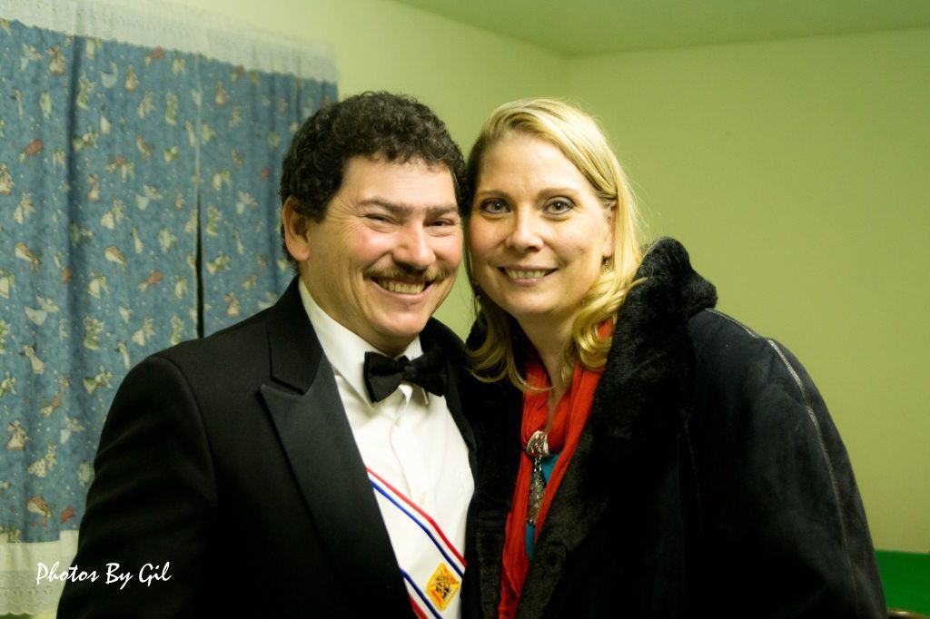 A smiling man in a black tuxedo and woman in a dark coat. 