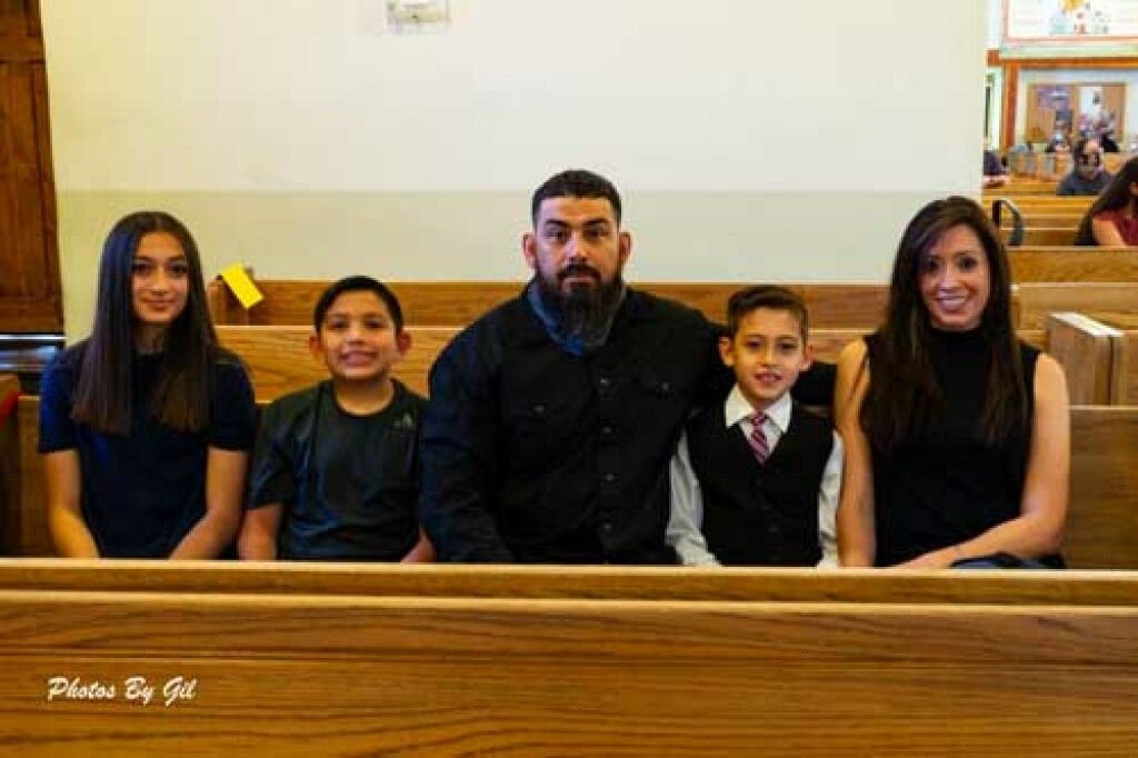 A family of five sits together on a church pew, posing for a photo.