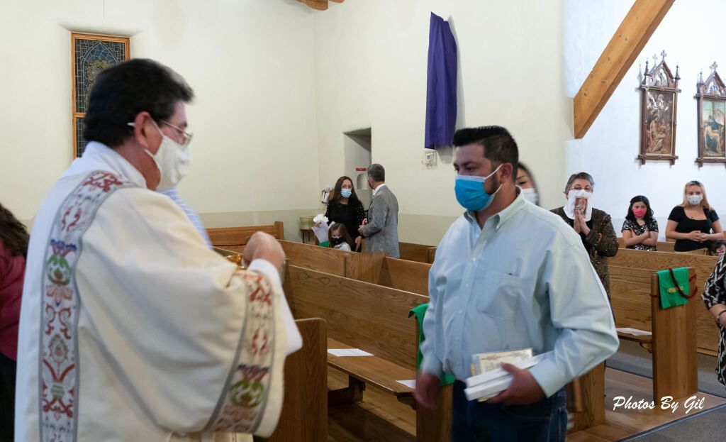 A masked priest hands a wafer to a man in a blue mask at a church. 