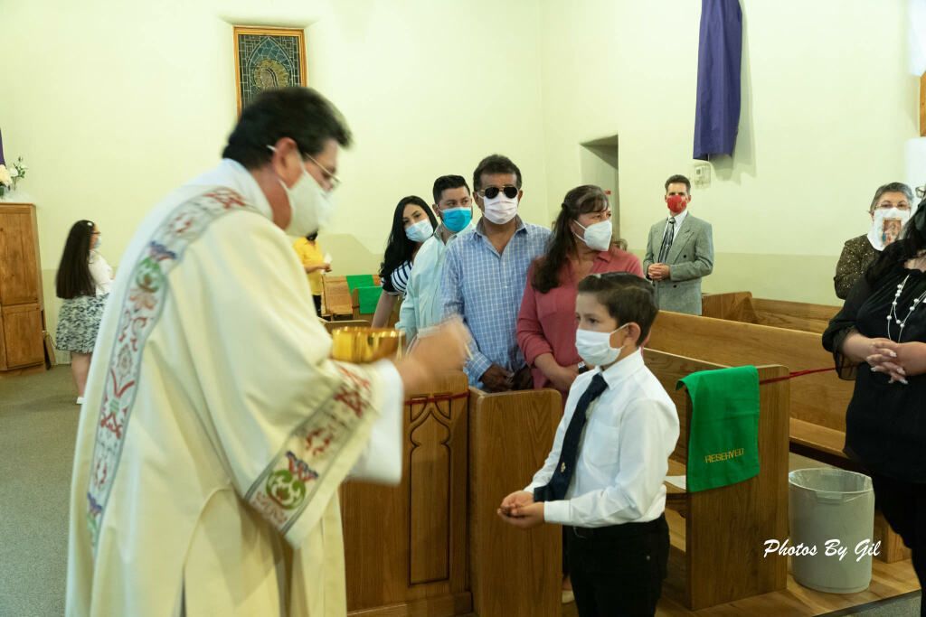 A priest wearing a mask gives communion to a young boy in a white shirt and tie. 