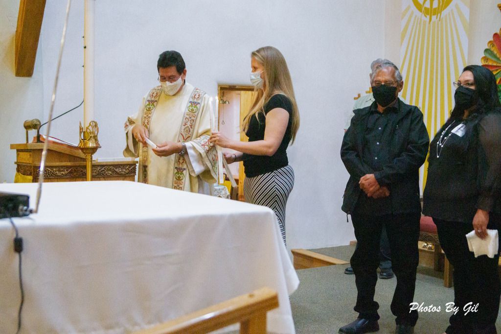 A priest in ceremonial robes stands beside a woman in a church, both wearing masks.