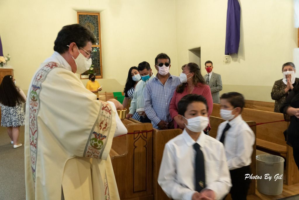 Priest in ornate vestment stands in church, serving communion to congregation.