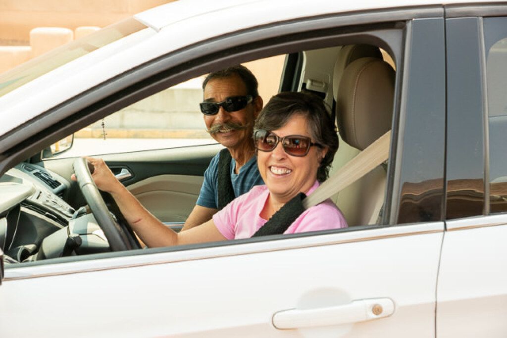 A smiling couple wearing sunglasses is seated in a white car. 
