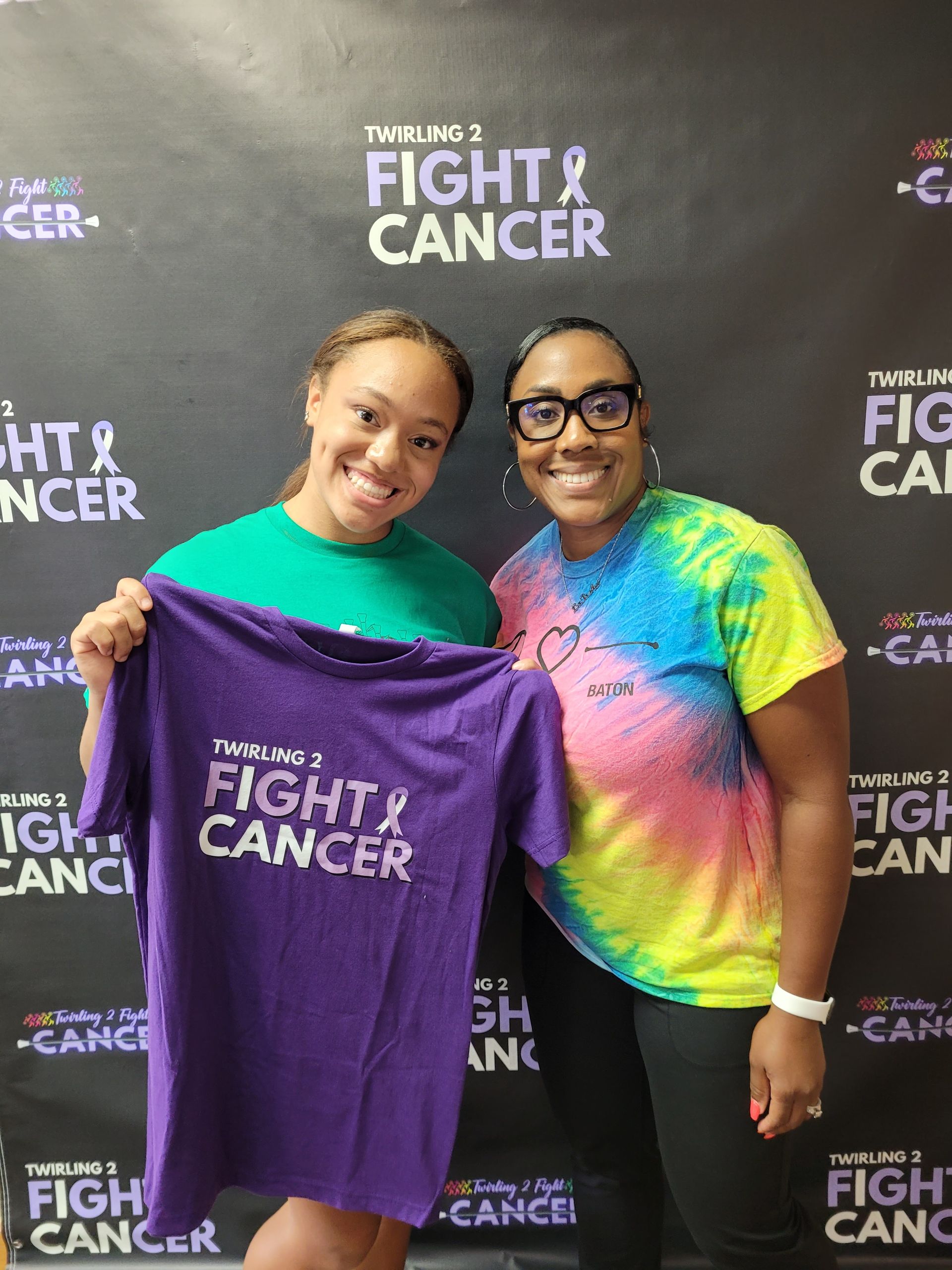 Two women are standing next to each other holding a purple shirt that says `` fight cancer ''.