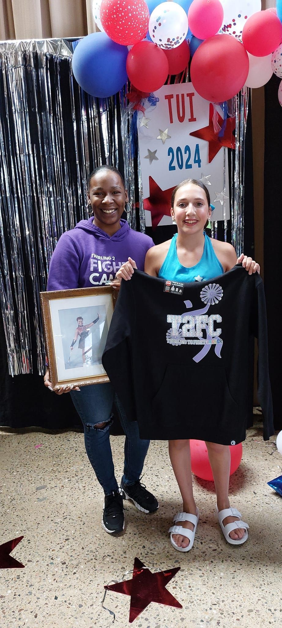 Two women are standing next to each other holding a shirt and a picture.