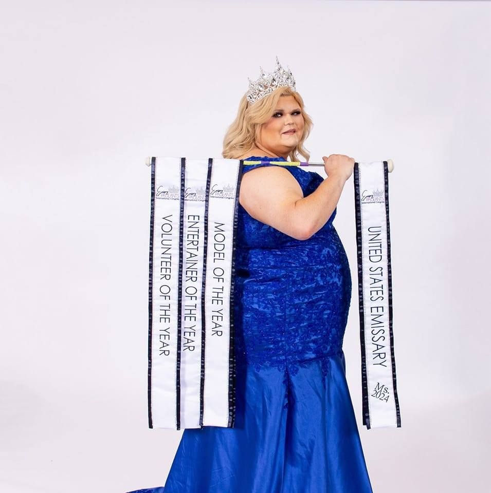 Person in a blue gown and crown, holding sashes that say