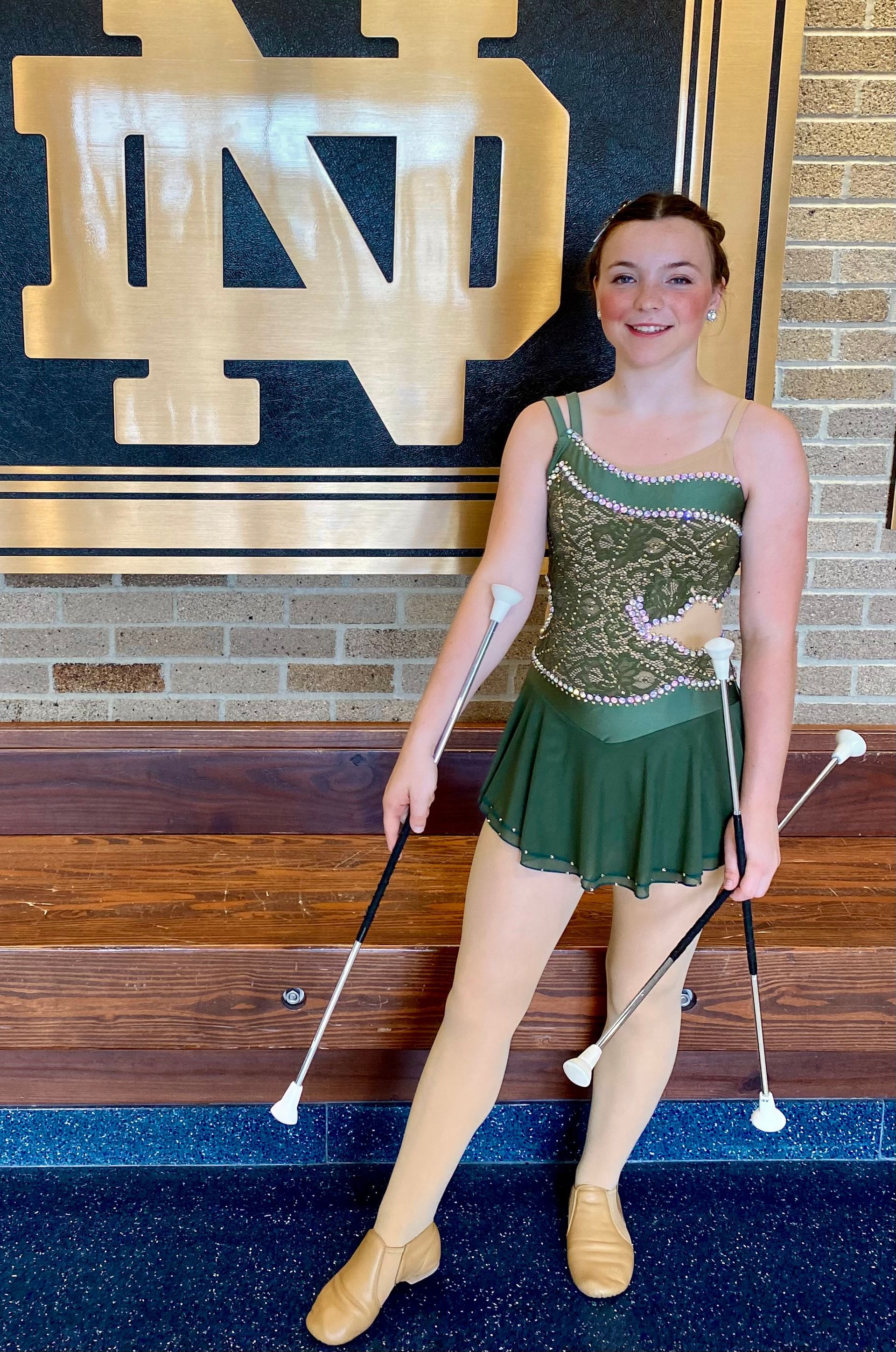 Woman in green and gold costume twirling batons at Notre Dame.