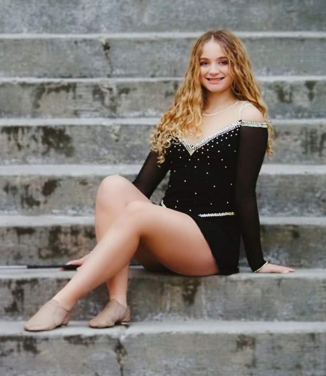 Woman in black dance outfit sits on concrete steps, smiling.