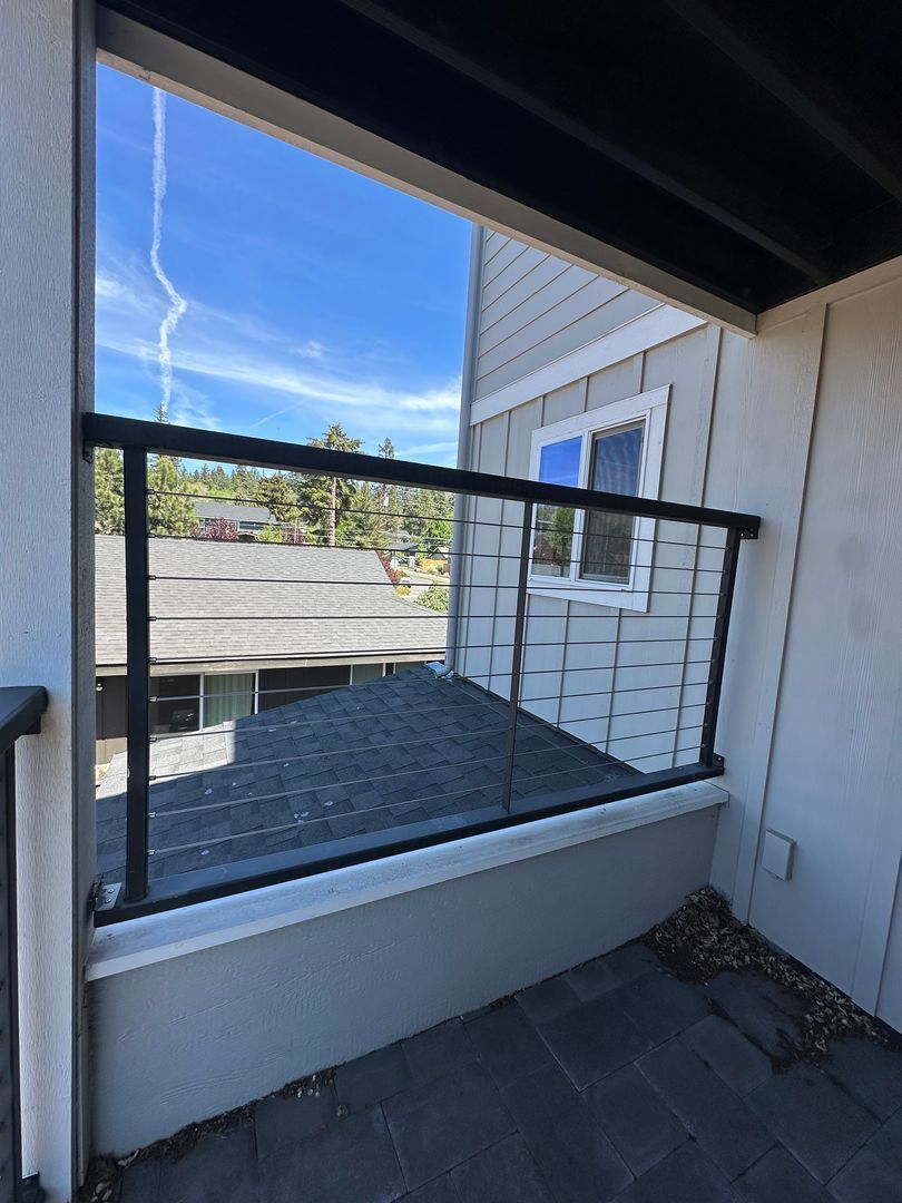 Balcony view through a screened opening, with blue sky, rooftops, and a dark railing.