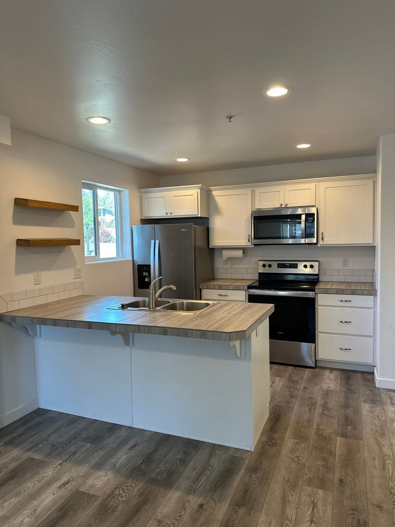 Bright modern kitchen with white cabinets, stainless appliances, island, and gray wood-look flooring