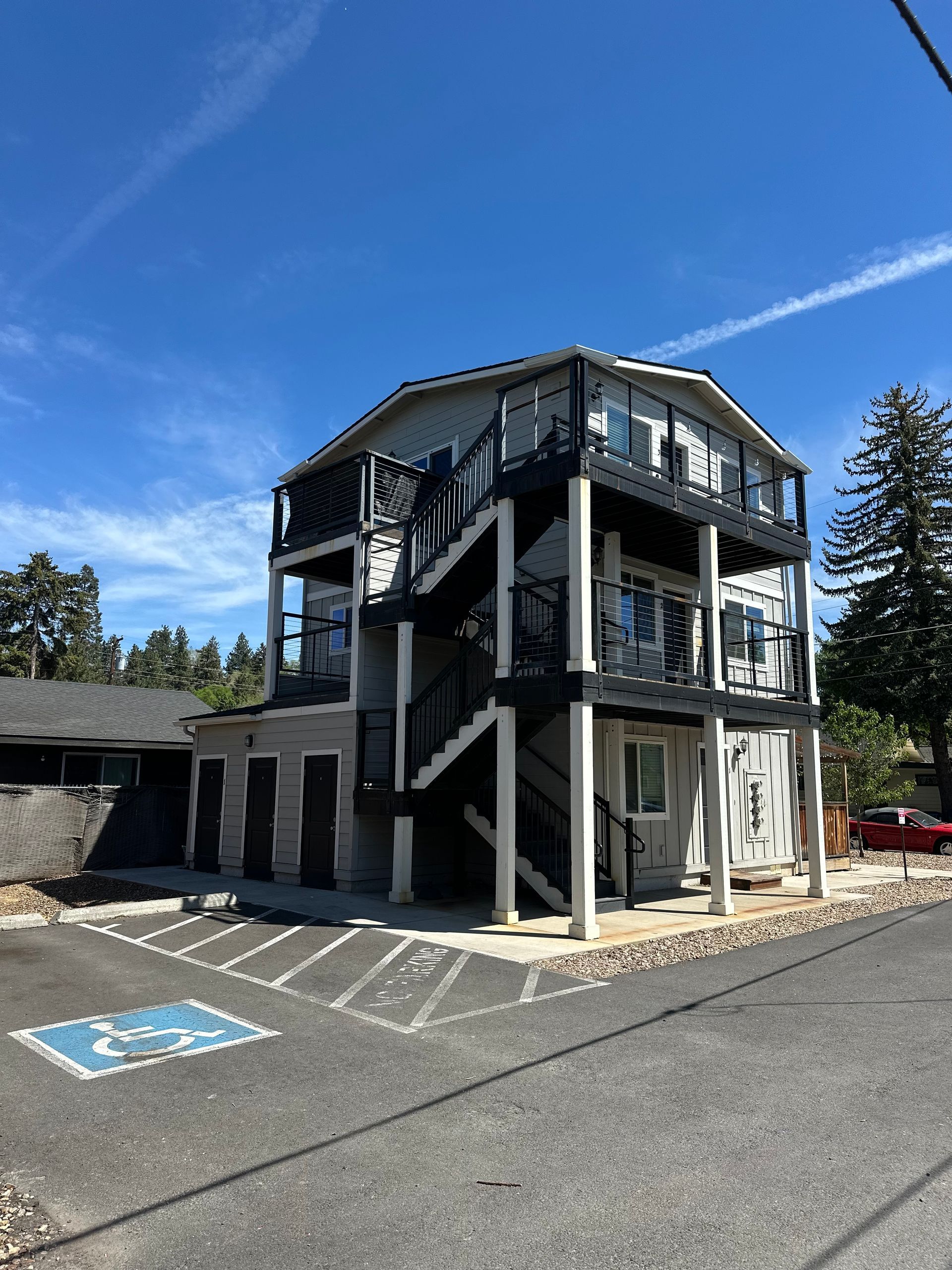 Two-story black-and-white building with exterior stairs and empty parking spaces under a blue sky.